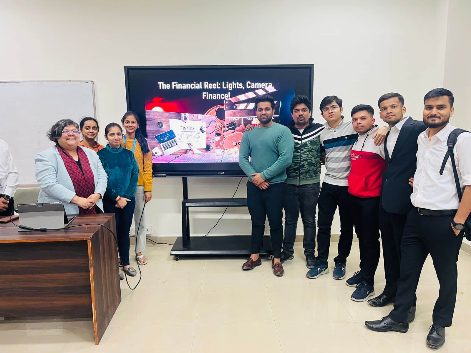 A cheerful group of MBA students and a faculty member standing in front of a presentation screen at Jaipuria Institute of Management, Ghaziabad, post an interactive learning session.