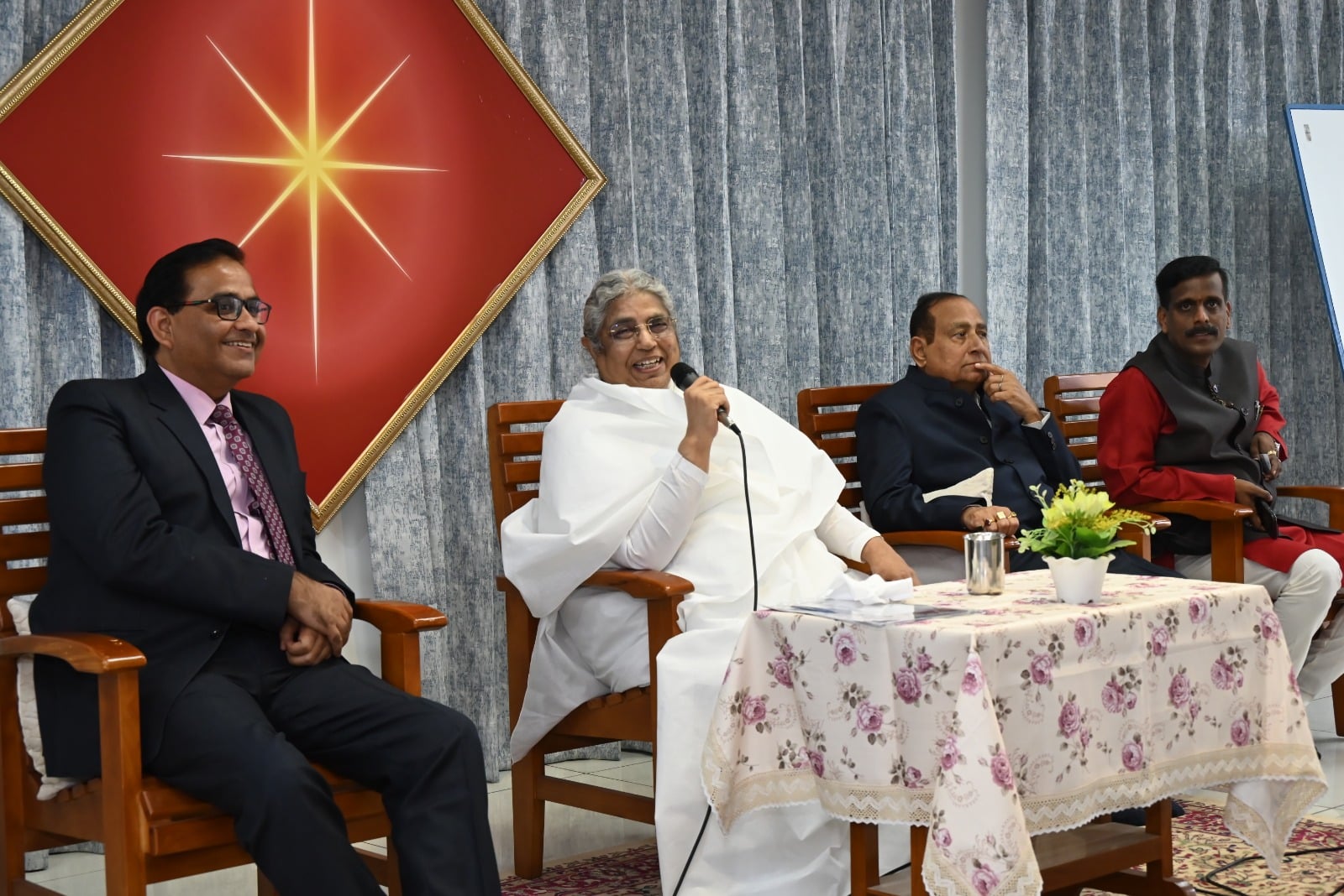 Asha Didi ji speaking to attendees at the Jaipuria Institute event, with other dignitaries listening attentively.