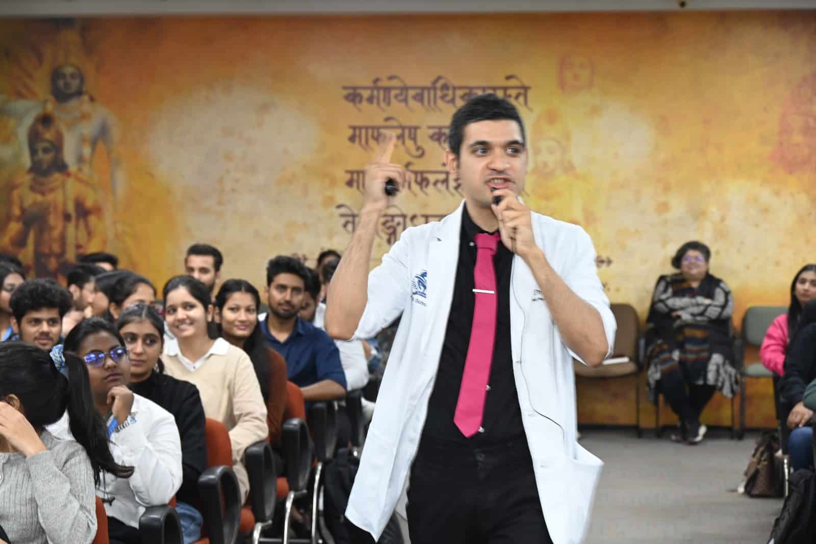 Dr. Faraz Harsini holding a microphone while giving a talk on alternative proteins, with a presentation slide in the background at the Jaipuria Institute of Management.