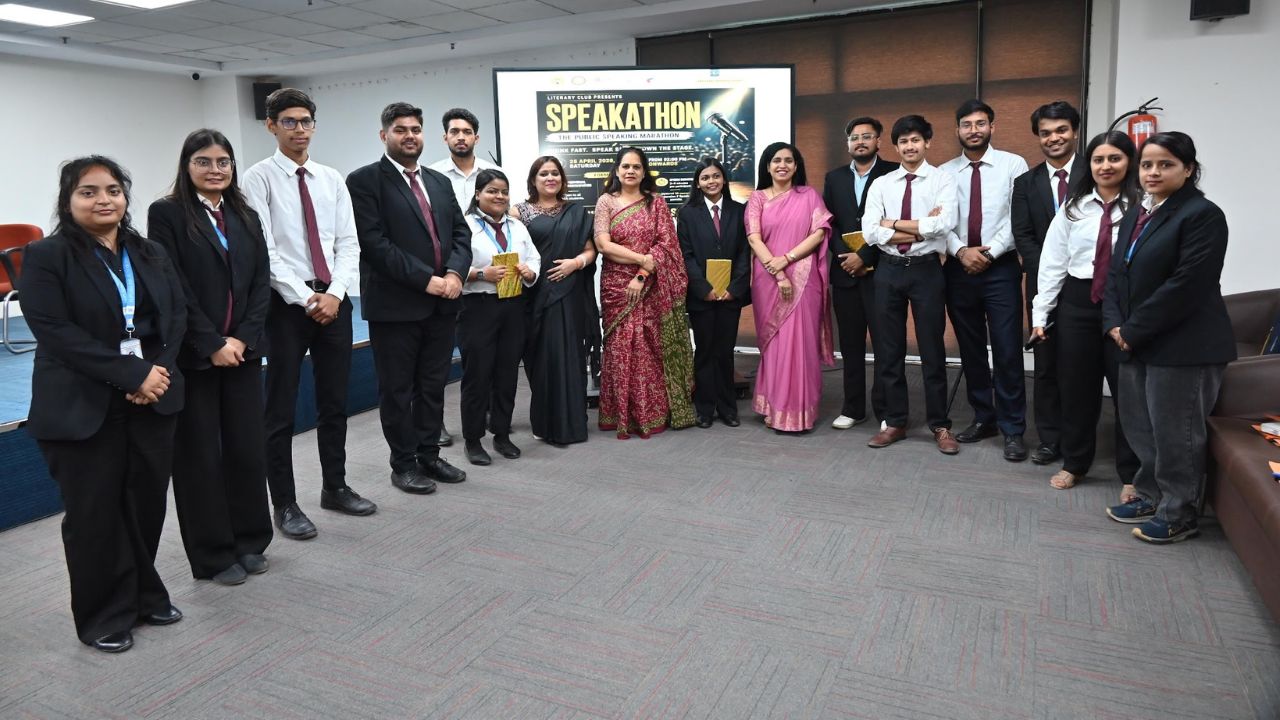 Group of students and mentors in formal attire posing in a conference room with a SPEAKATHON poster on the screen behind them, suggesting a campus event photo.