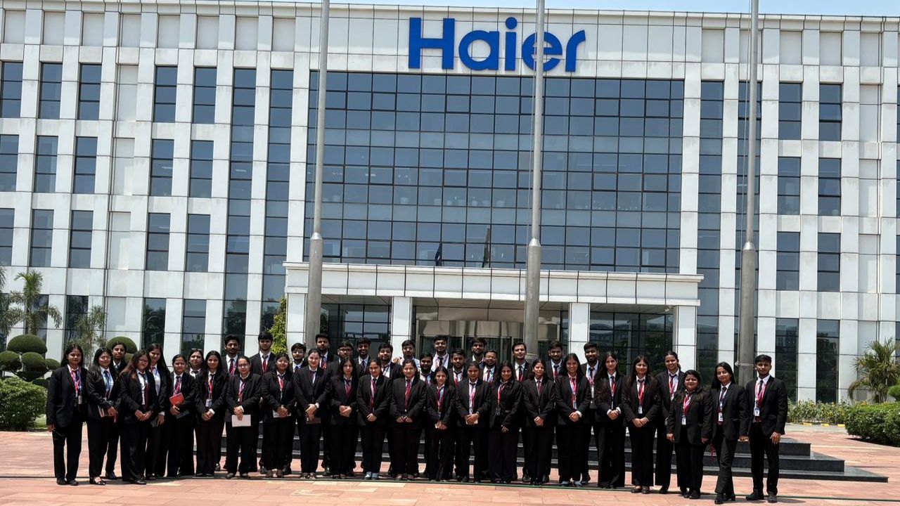 Group of professionally dressed people standing in a line outside a Haier building, posing for a company photo.