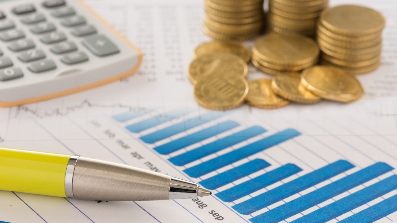 Blue bar chart on a finance report with a yellow pen and stacks of coins nearby, indicating budgeting data
