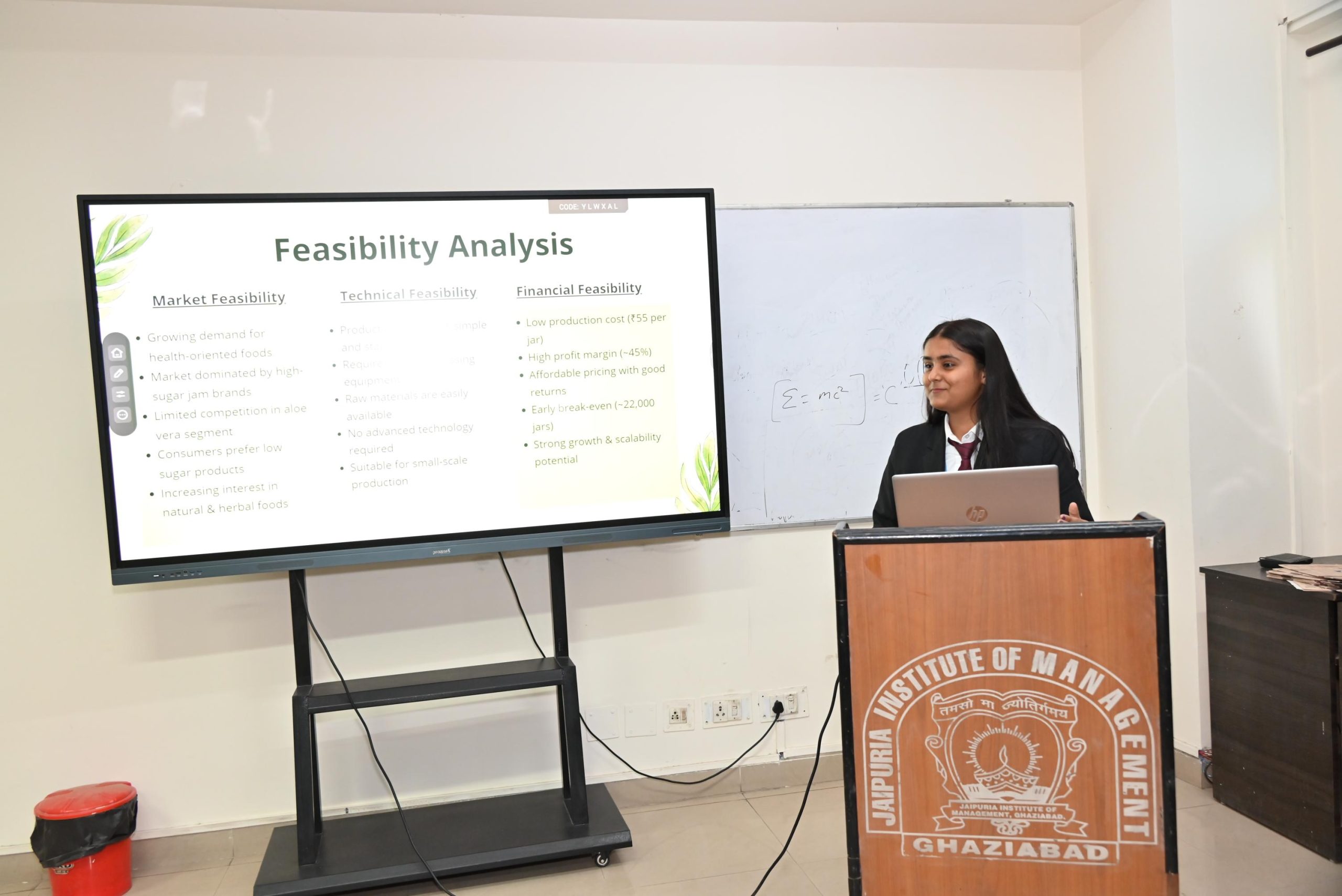 Workshop on Protecting IPR and IP Management for Startups 2026 3 - Jaipuria Institute of Management, Indirapuram Ghaziabad Presenter standing beside a large monitor showing a Feasibility Analysis slide in a classroom.