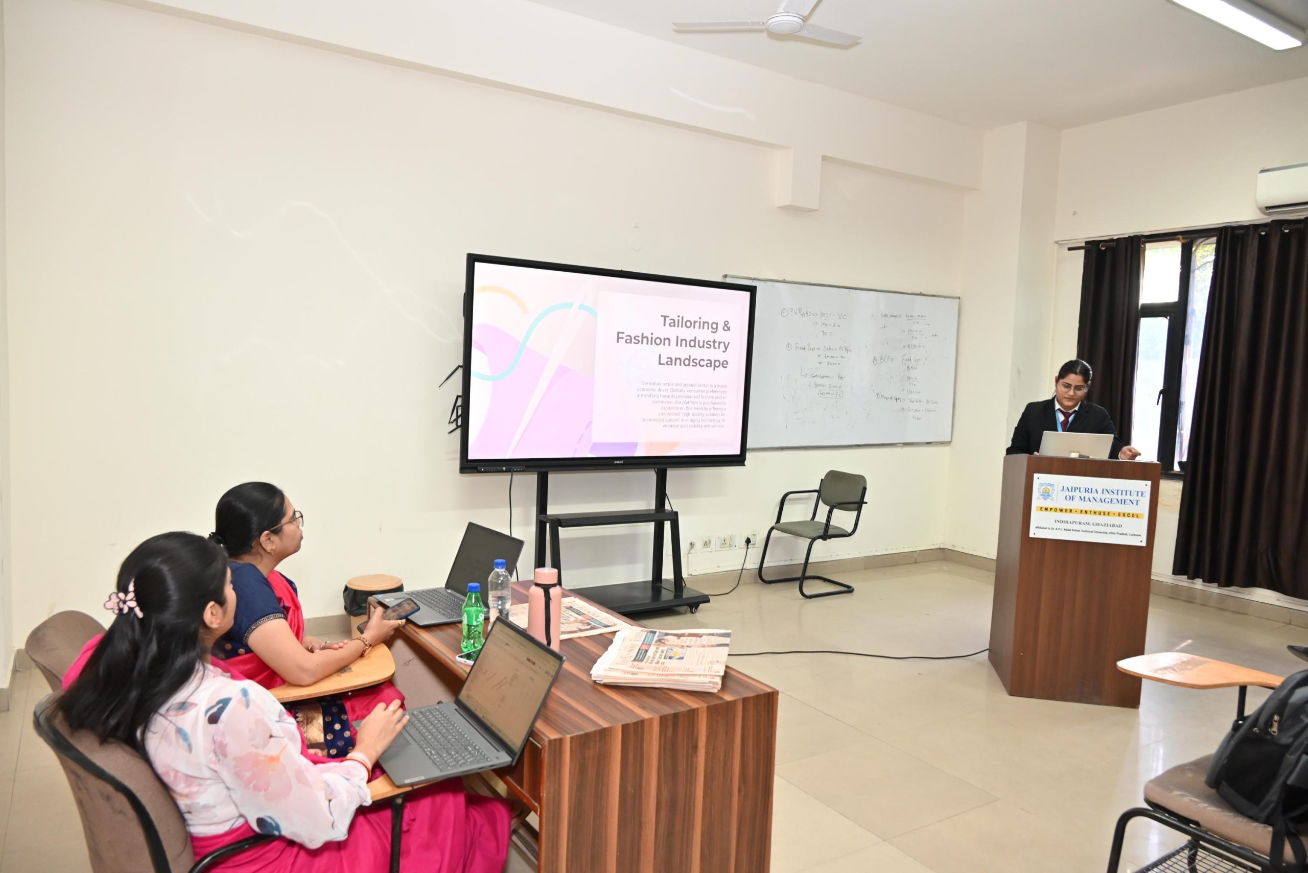 Workshop on Protecting IPR and IP Management for Startups 2026 4 - Jaipuria Institute of Management, Indirapuram Ghaziabad Lecture room scene with a presenter at a podium beside a screen showing 'Tailoring & Fashion Industry Landscape' while students use laptops at desks.