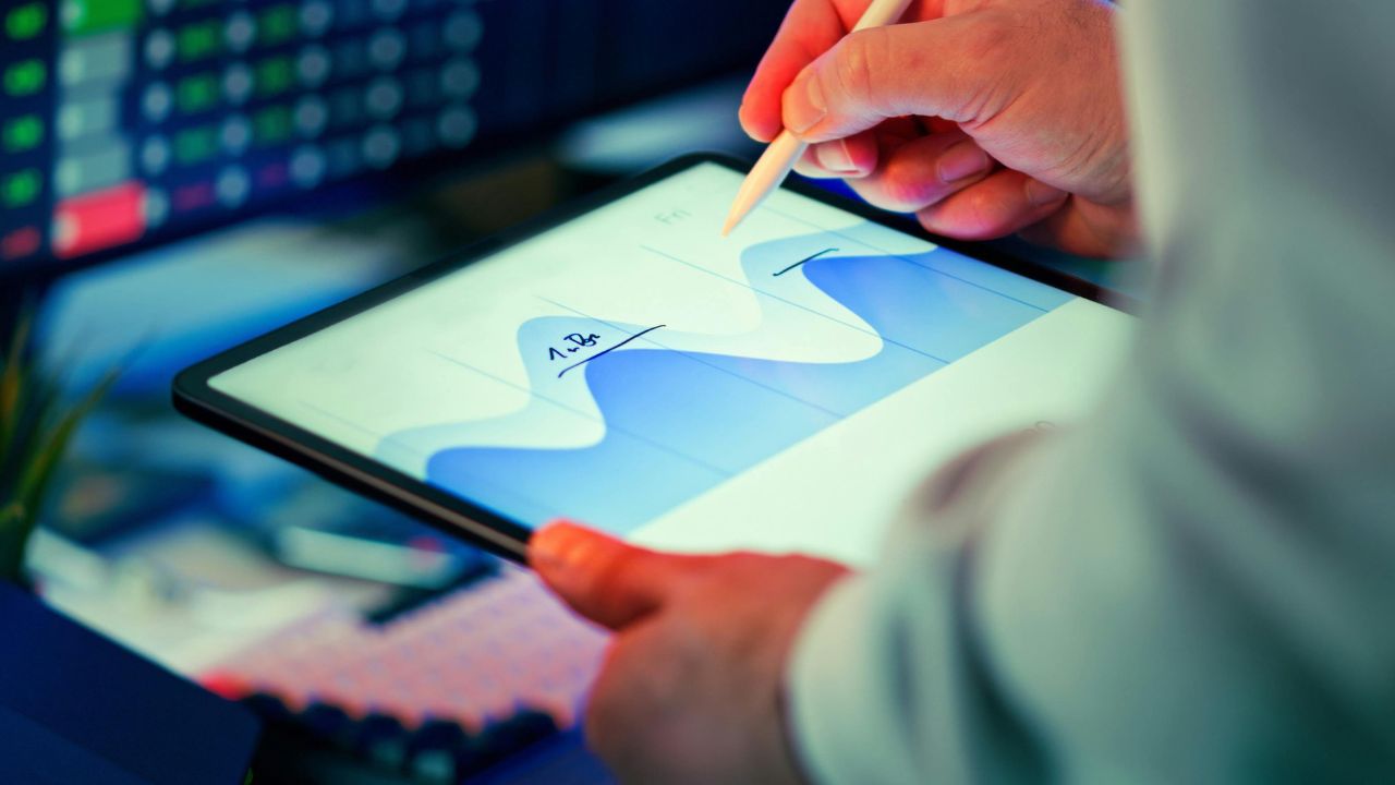 Person using a tablet with a stylus to edit a blue and white wave chart on screen on a desk surface.