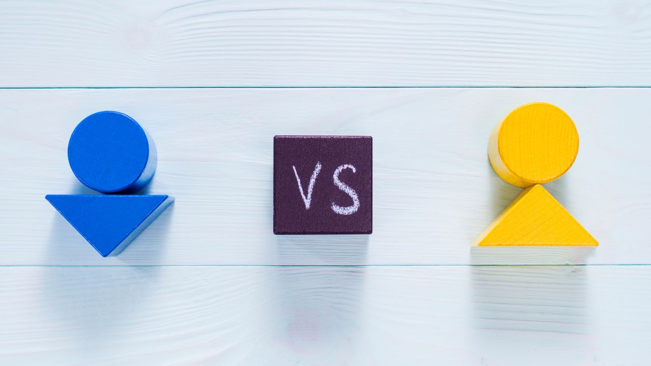 Two abstract wooden figures, blue on the left and yellow on the right, face off with a dark square 'VS' in the center on a light wooden background.