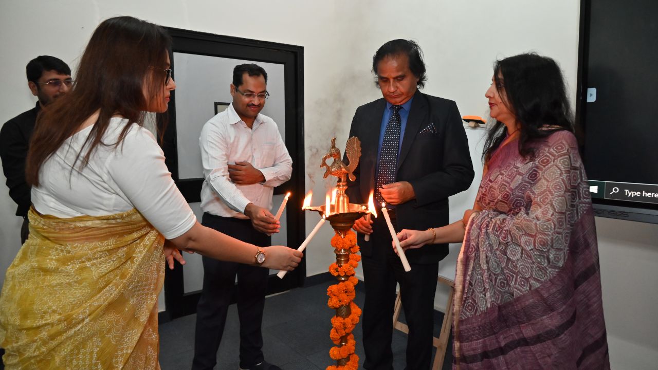 Report on Day 1 of the 5-Day Faculty Development Program 2 - Jaipuria Institute of Management, Indirapuram Ghaziabad Group of five people lighting a ceremonial lamp during an inauguration in an office setting, with orange marigold garlands nearby