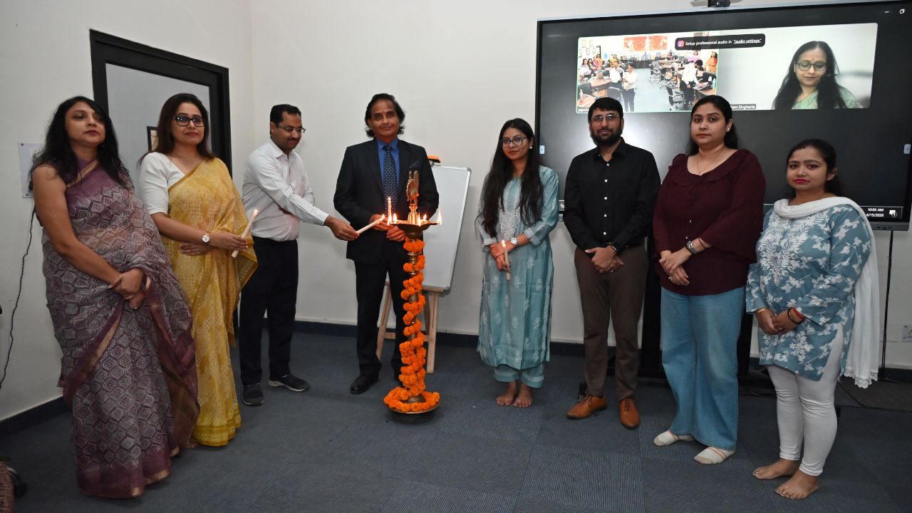 Report on Day 1 of the 5-Day Faculty Development Program 3 - Jaipuria Institute of Management, Indirapuram Ghaziabad Group of colleagues in a ceremony around a lit traditional diya lamp in an office space, marigold garland on the stand, with a screen in the background.