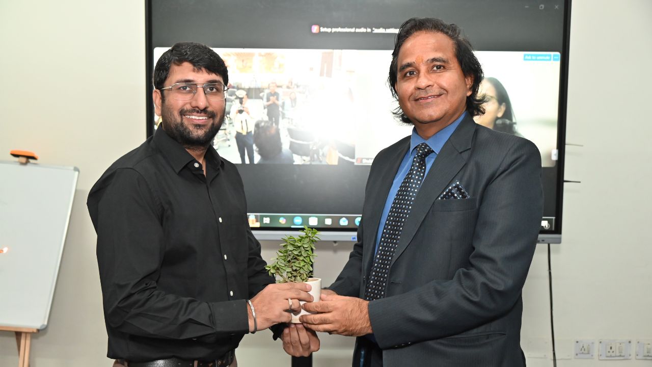 Report on Day 1 of the 5-Day Faculty Development Program 4 - Jaipuria Institute of Management, Indirapuram Ghaziabad Two men in a presentation room exchange a small potted plant, smiling at the camera.