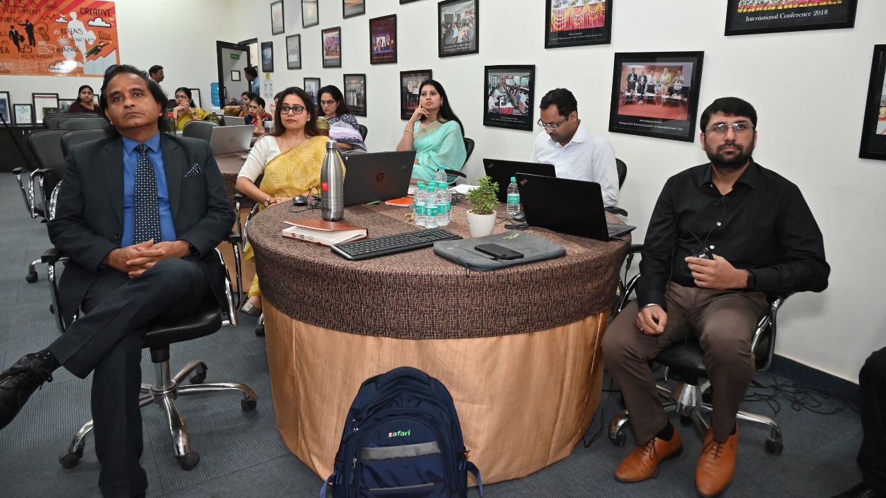 Report on Day 1 of the 5-Day Faculty Development Program 5 - Jaipuria Institute of Management, Indirapuram Ghaziabad Group of professionals in a conference room around a round table with laptops and water bottles, preparing for a meeting.