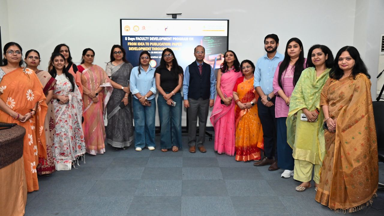 Group of professionals in colorful Indian attire posing for a photo in front of a presentation screen in a conference room.