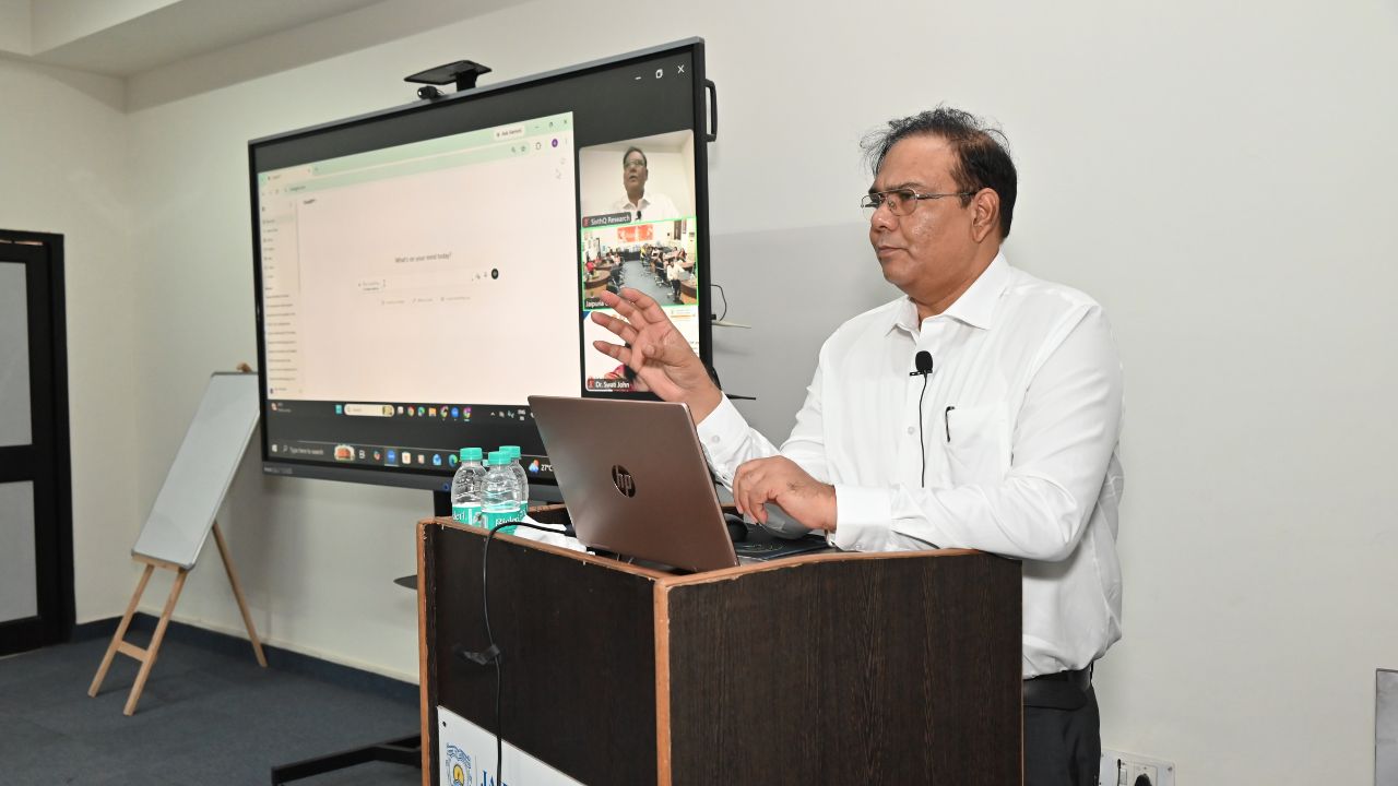 Report on Day 5 and Valedictory Session of the 5-Day Faculty Development Program 1 - Jaipuria Institute of Management, Indirapuram Ghaziabad Speaker in a white shirt delivers a lecture at a podium; a large screen shows a video conference and slides behind him.