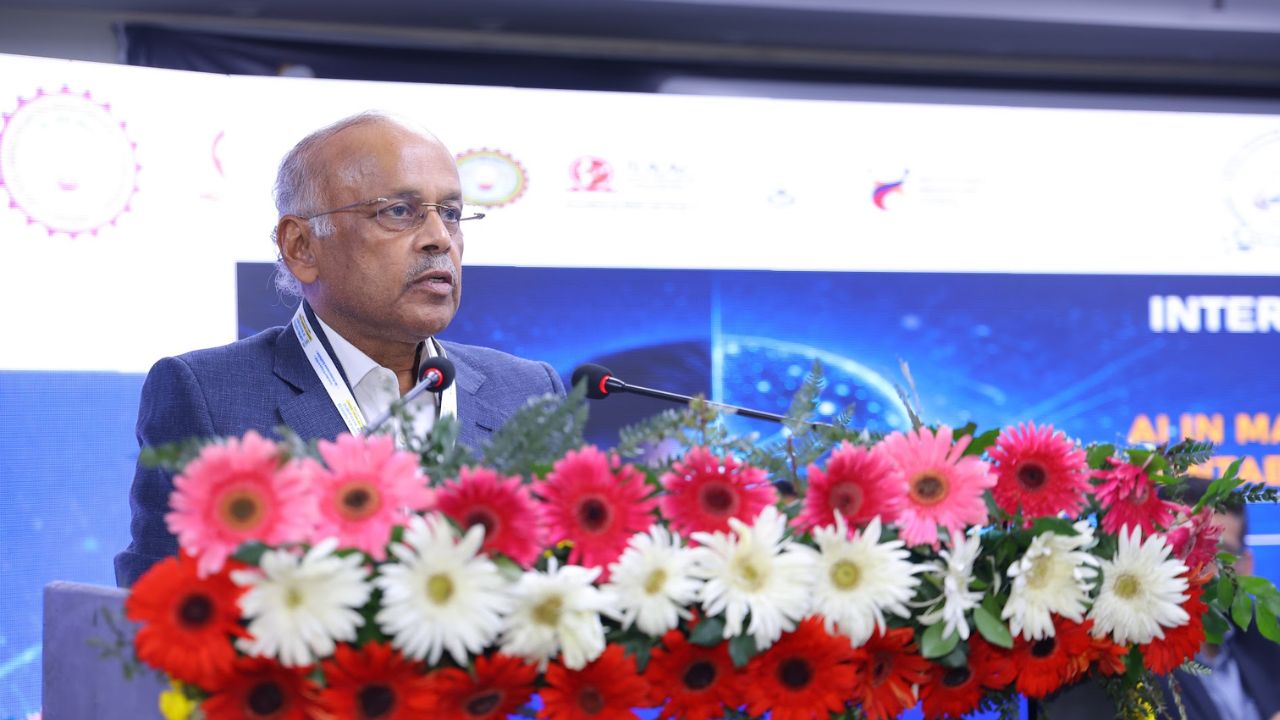 AIM-PEACE 2026_ International AI Conference at Jaipuria MBA 4 - Jaipuria Institute of Management, Indirapuram Ghaziabad Man in a navy suit giving a speech at a podium covered with pink, red, and white flowers.