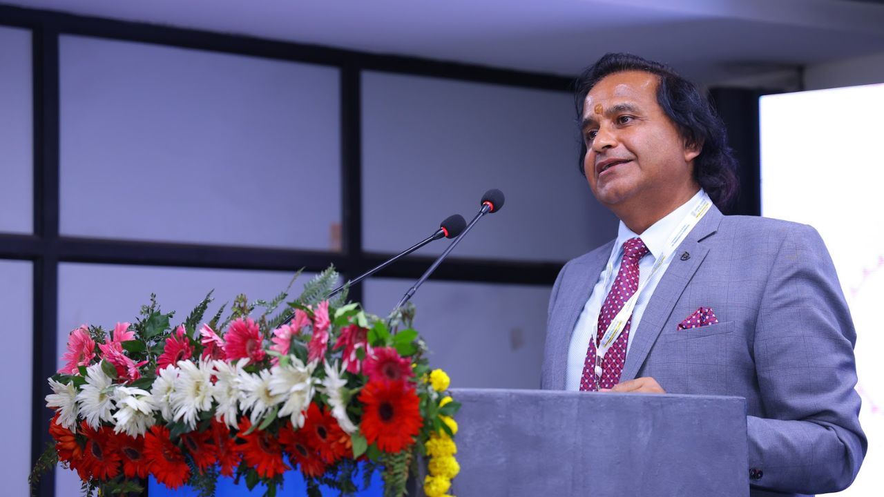 AIM-PEACE 2026_ International AI Conference at Jaipuria MBA 5 - Jaipuria Institute of Management, Indirapuram Ghaziabad Man in a gray suit delivering a speech at a podium with a vibrant flower arrangement in front of him.