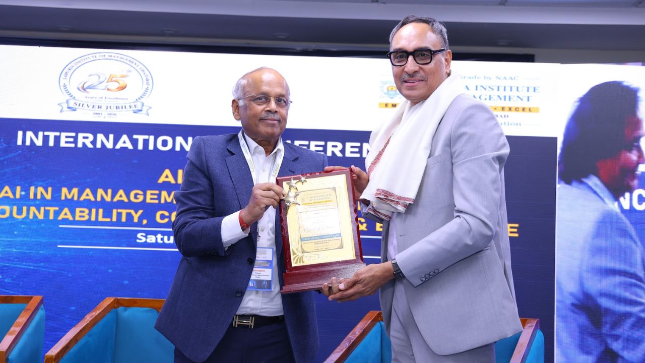 AIM-PEACE 2026_ International AI Conference at Jaipuria MBA 6 - Jaipuria Institute of Management, Indirapuram Ghaziabad Two men in suits exchange a wooden plaque on a stage during an award ceremony, with a blue backdrop and conference banners behind them.