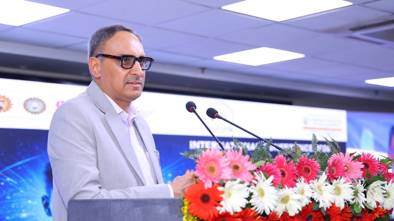 AIM-PEACE 2026_ International AI Conference at Jaipuria MBA 9 - Jaipuria Institute of Management, Indirapuram Ghaziabad Man in a light gray suit speaking at a podium decorated with pink, red, and white flowers during a conference.