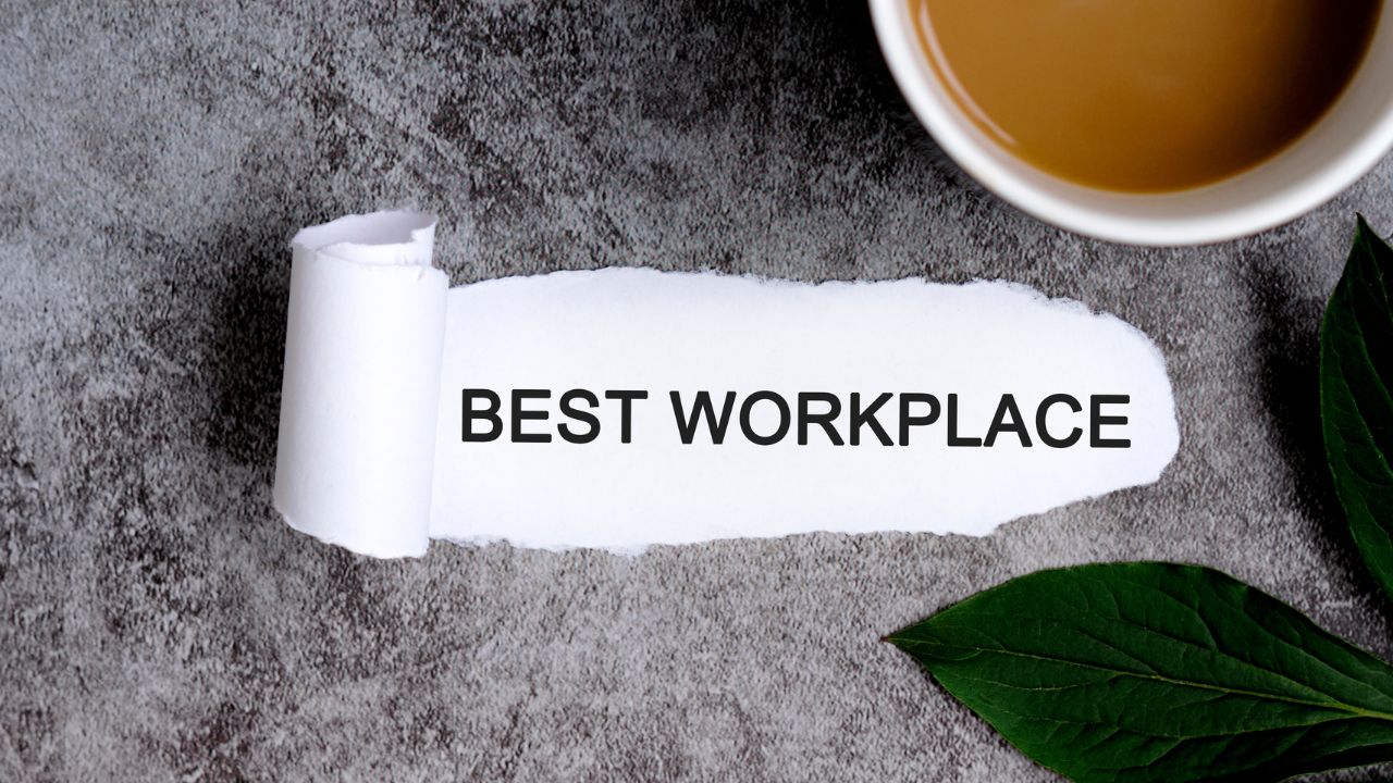 Torn white paper reads BEST WORKPLACE on a gray textured surface, with a cup of tea and green leaves nearby.