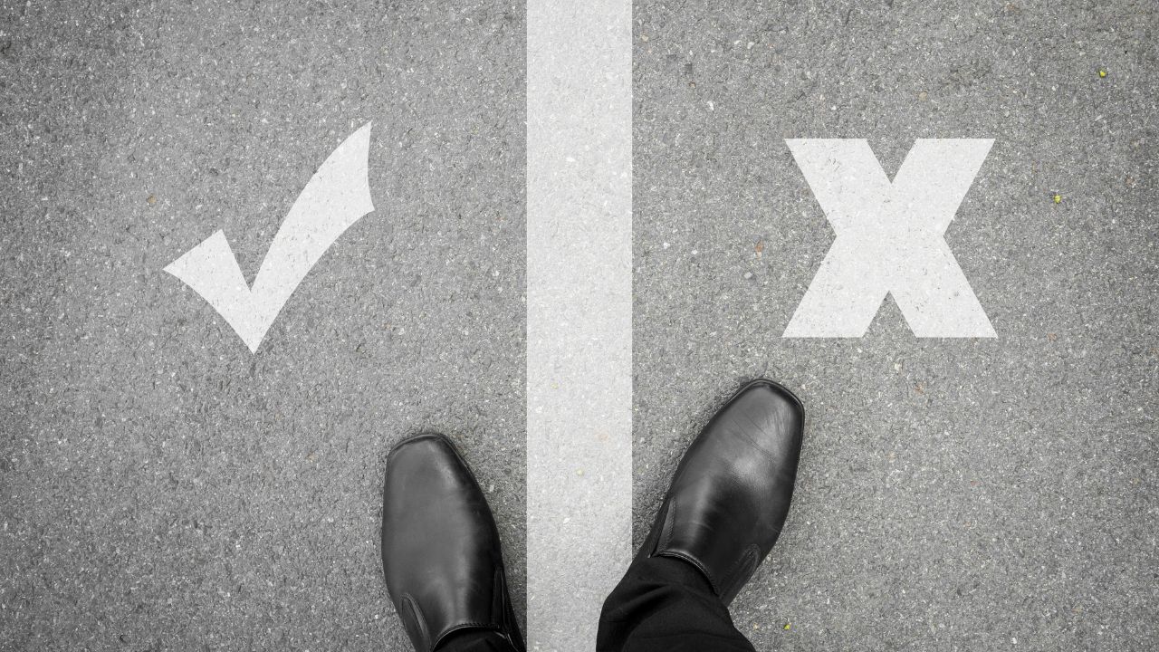 Feet on pavement between a white checkmark on the left and a white X on the right, symbolizing a yes/no choice.