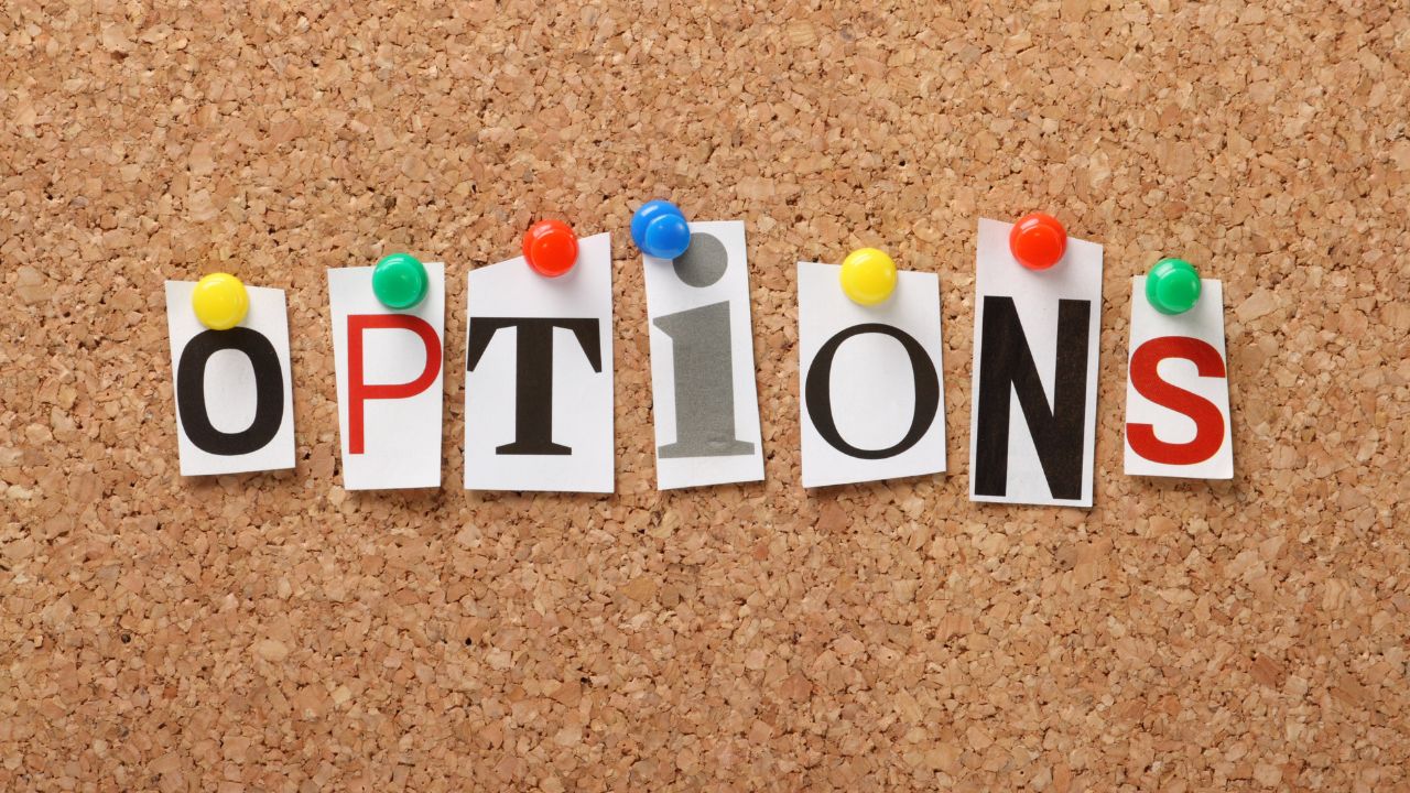 Letters spelling OPTIONS pinned to a corkboard with colorful push pins, suggesting choices or settings.