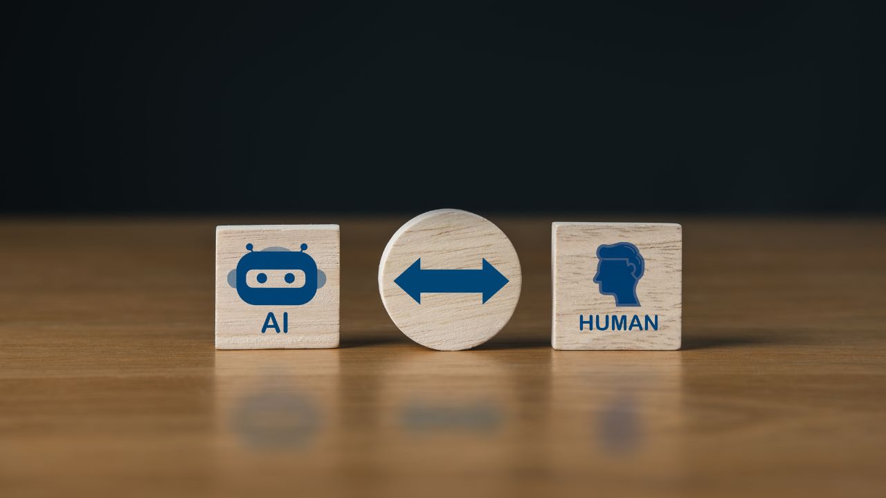 Wooden blocks show AI with a robot icon, a central double-headed arrow, and a HUMAN block with a head silhouette—illustrating human–AI collaboration.