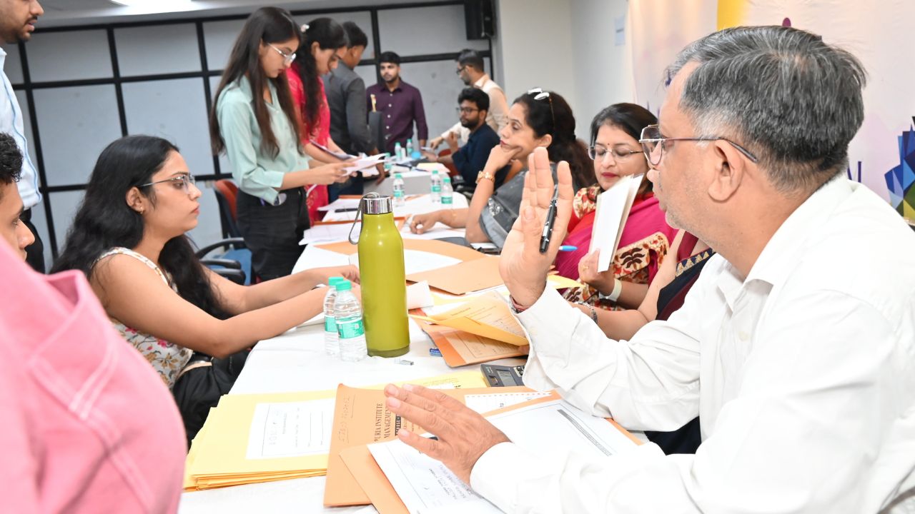 Day 1 of Reporting Day 3 - Jaipuria Institute of Management, Indirapuram Ghaziabad Panel of professionals seated at a long table reviewing documents as candidates hand over papers inked with folders and bottles nearby