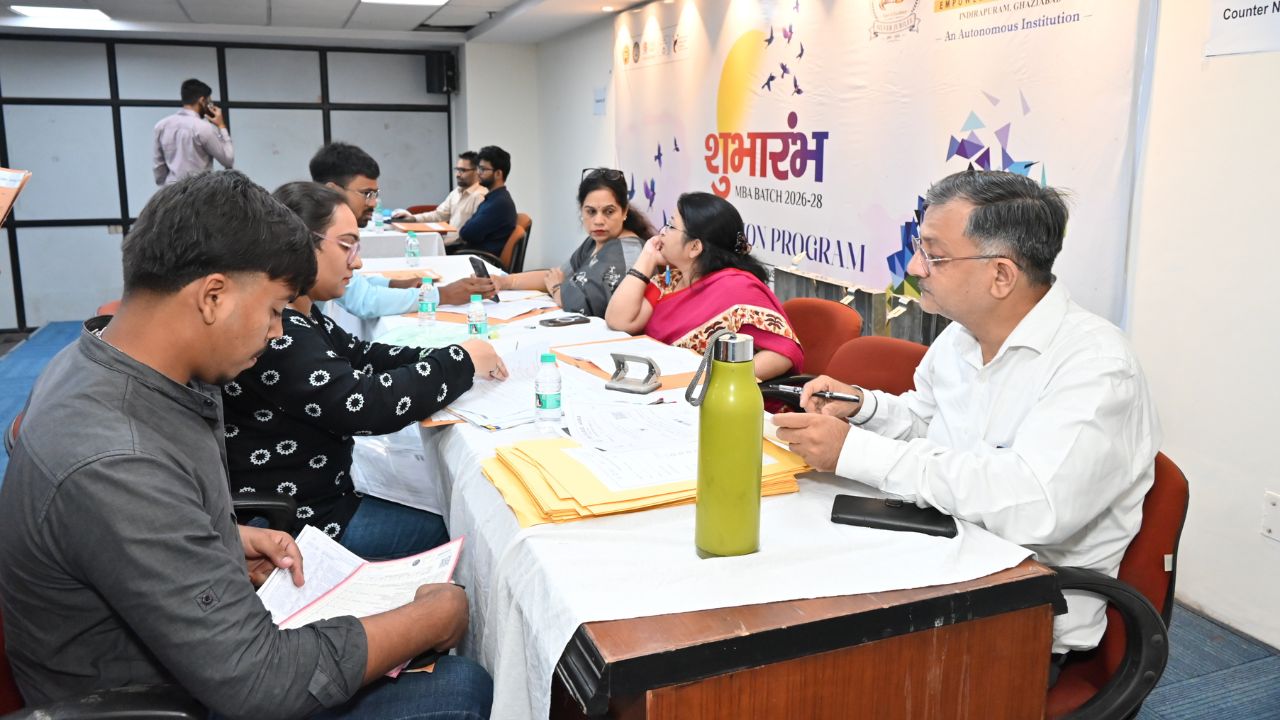 Day 1 of Reporting Day 6 - Jaipuria Institute of Management, Indirapuram Ghaziabad Panel of instructors and participants seated at a long table, reviewing documents during a program enrollment event, with a banner in the background.