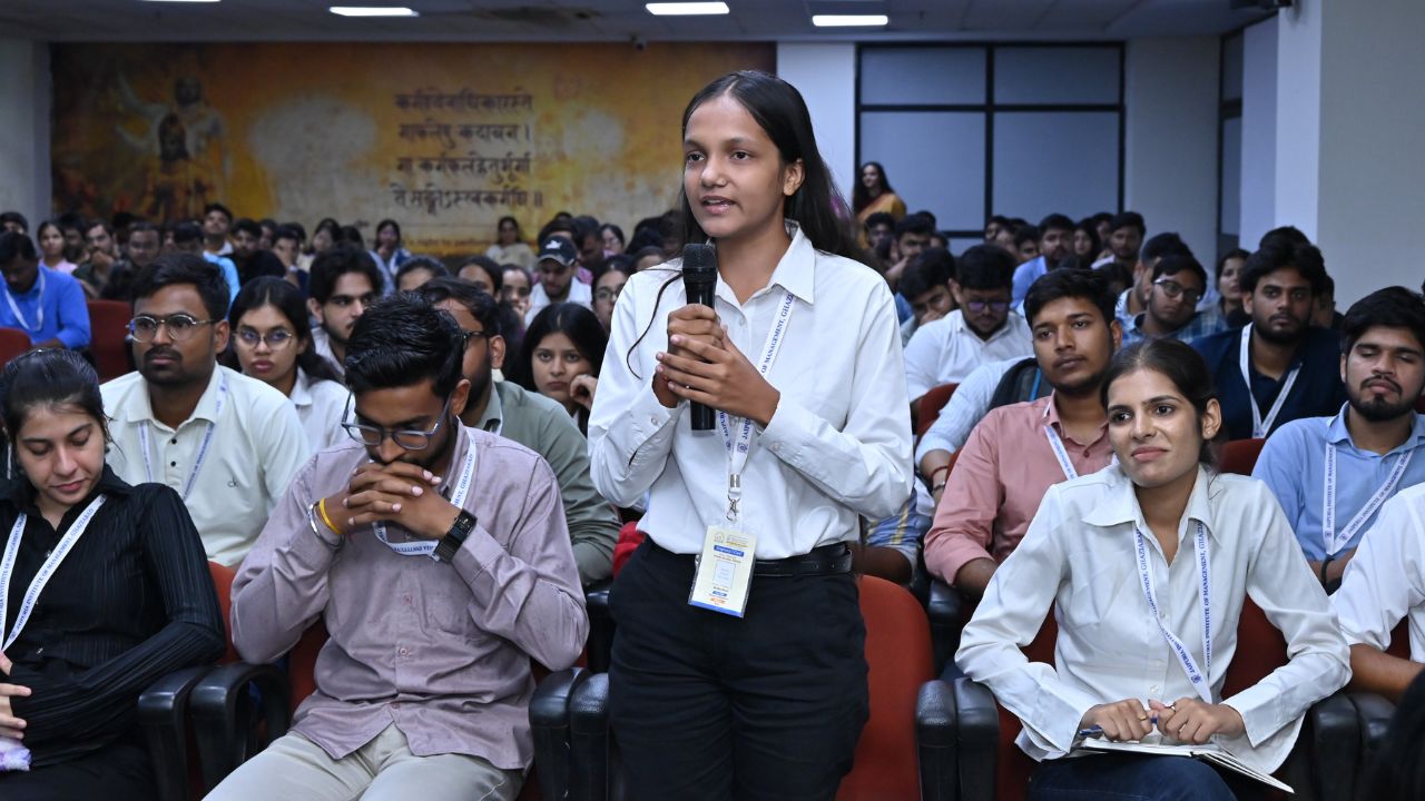 IIC Panel Discussion on Innovation & Startup Ecosystem (4) - Jaipuria Institute of Management, Indirapuram Ghaziabad Student raises a question, standing with a mic in a classroom full of peers during a Q&A session.