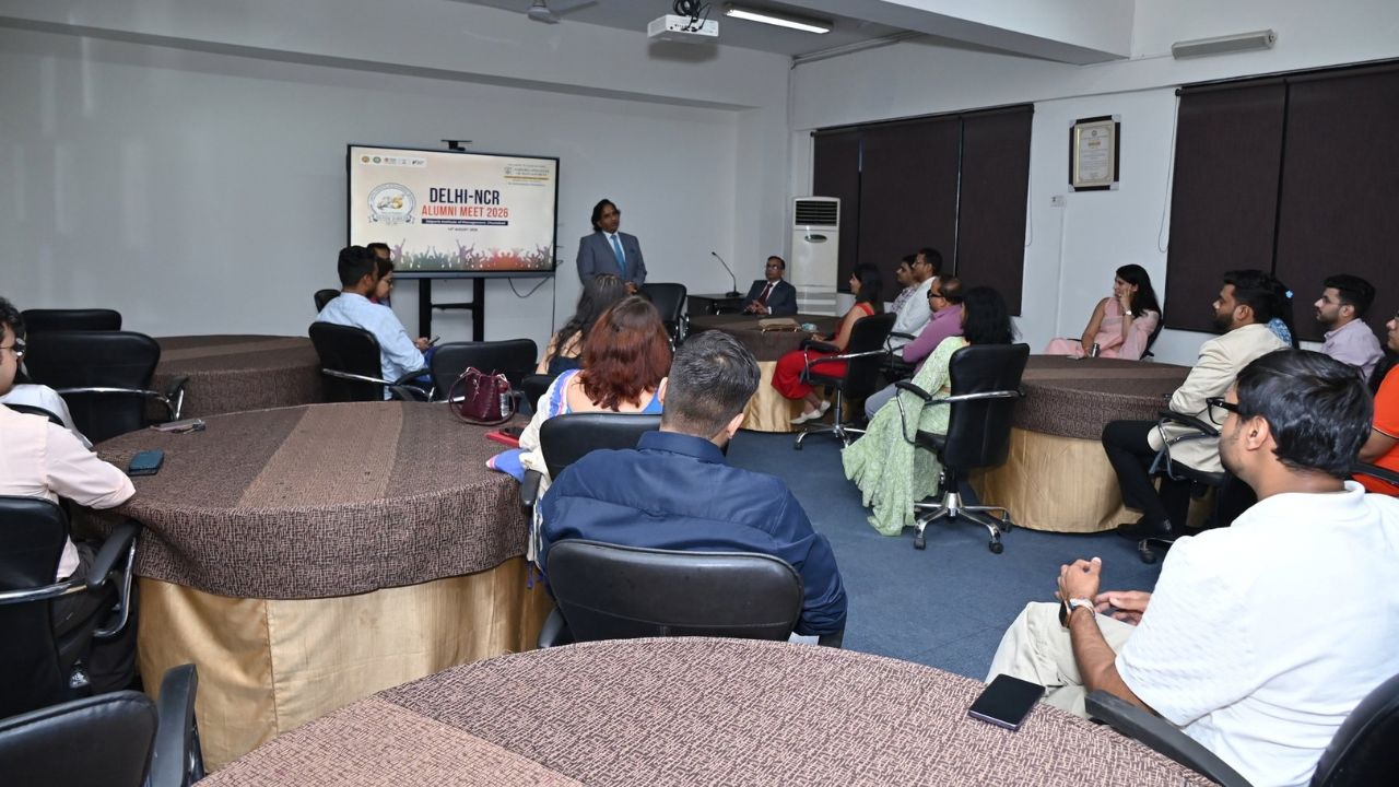 Alumni Chapter Meet NCR Chapter_ Reconnecting Legacy Celebrating Success 3 - Jaipuria Institute of Management, Indirapuram Ghaziabad Speaker in a suit presenting to professionals in a conference room; screen reads 'Delhi-NCR Alumni Meet 2026'.