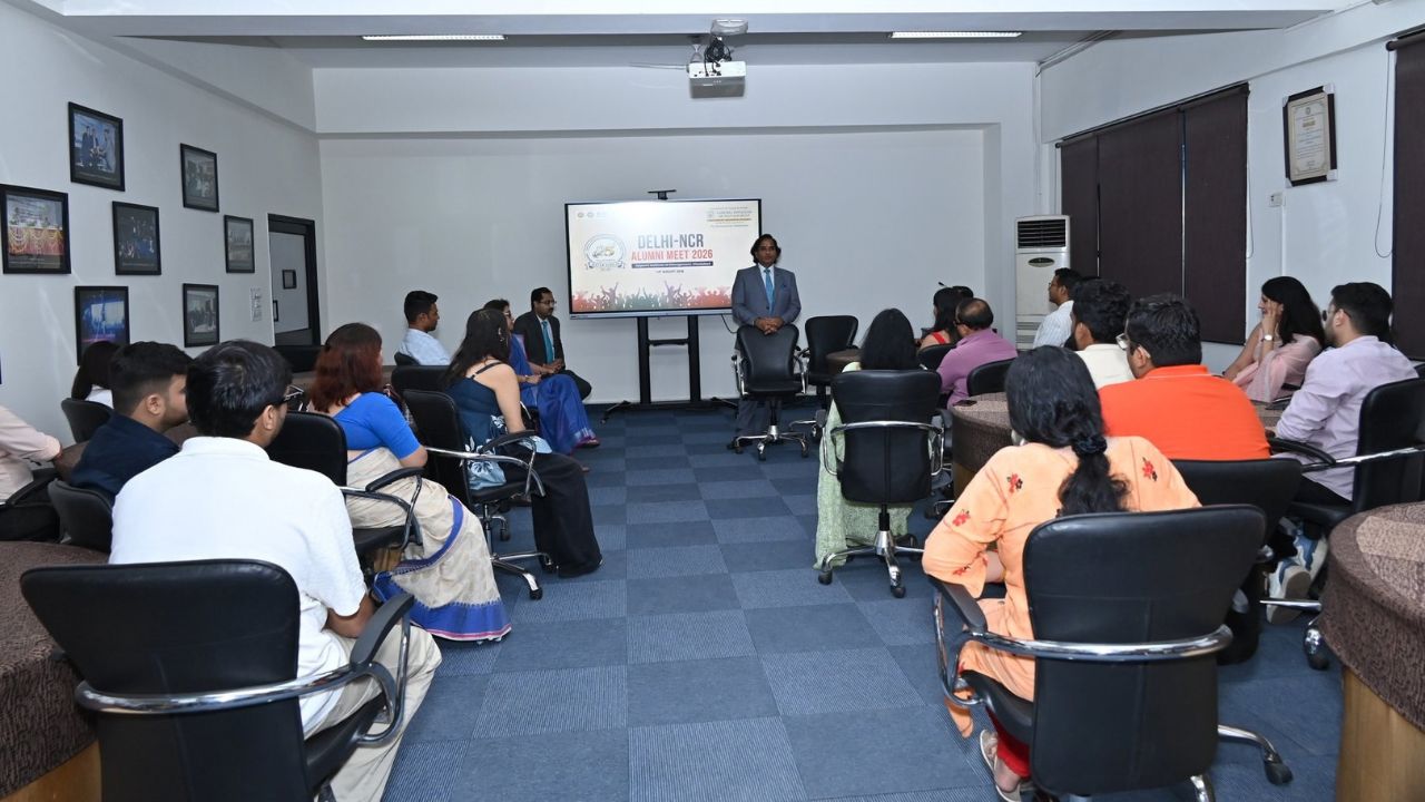 Alumni Chapter Meet NCR Chapter_ Reconnecting Legacy Celebrating Success 5 - Jaipuria Institute of Management, Indirapuram Ghaziabad Speaker in a gray suit addresses a seated audience in a seminar room; screen shows 'Delhi-NCR Alumni Meet 2026'.
