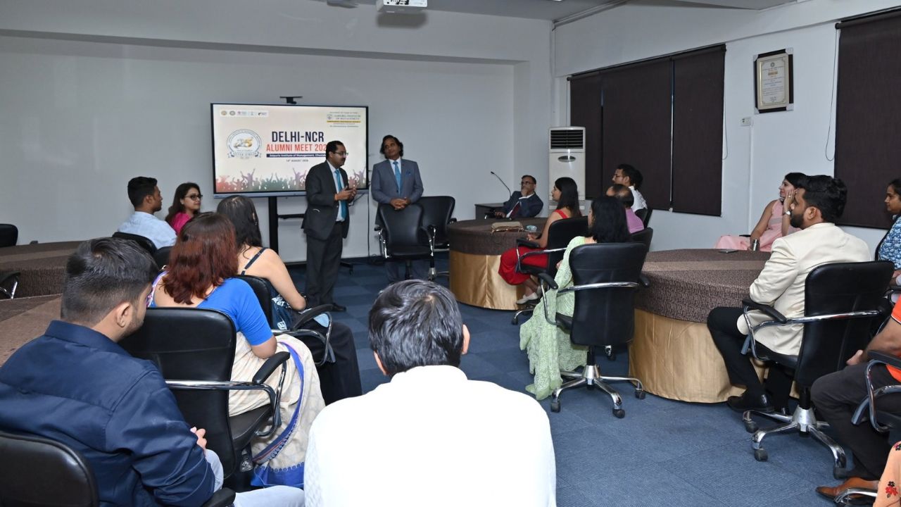 Alumni Chapter Meet NCR Chapter_ Reconnecting Legacy Celebrating Success 7 - Jaipuria Institute of Management, Indirapuram Ghaziabad Audience seated in a conference room listening to two men presenting at a Delhi-NCR Alumni Meet; screen displays event banner.