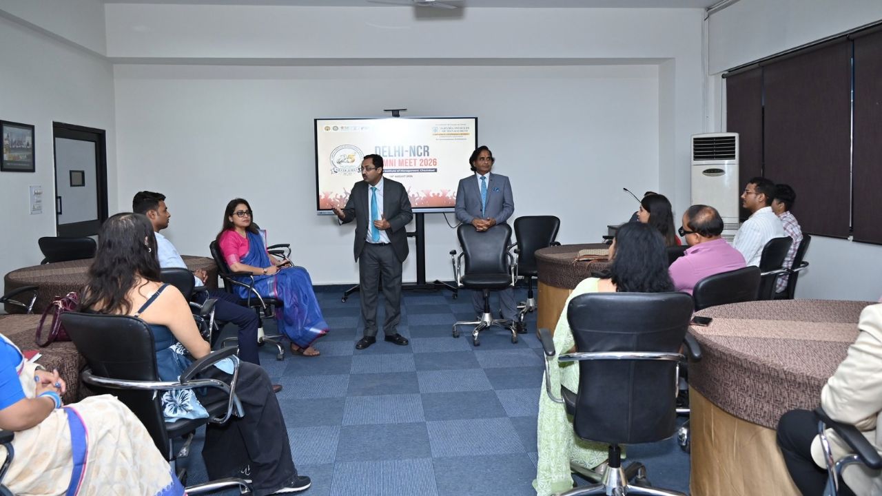 Alumni Chapter Meet NCR Chapter_ Reconnecting Legacy Celebrating Success 8 - Jaipuria Institute of Management, Indirapuram Ghaziabad Group of professionals seated around circular tables in a meeting room, watching a presenter at the front with a screen behind them.