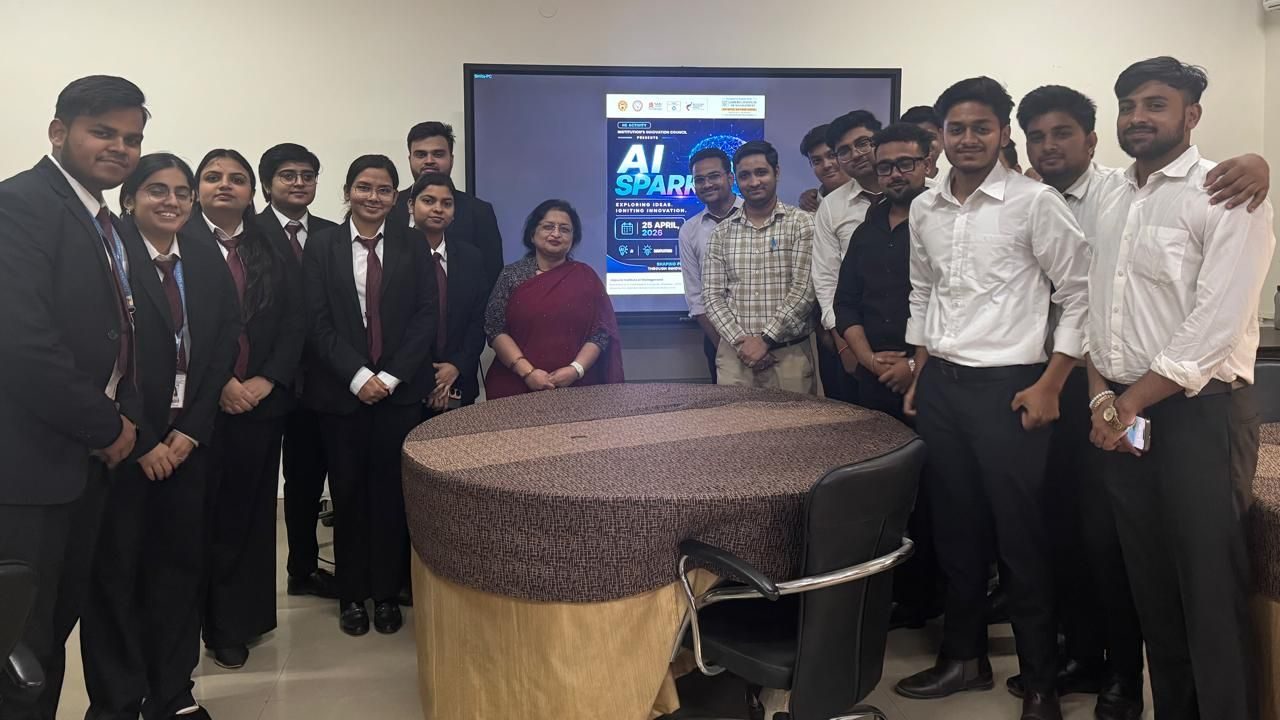 Group of students in formal attire posing around a round conference table, with a screen showing an AI SPARK poster in the background.