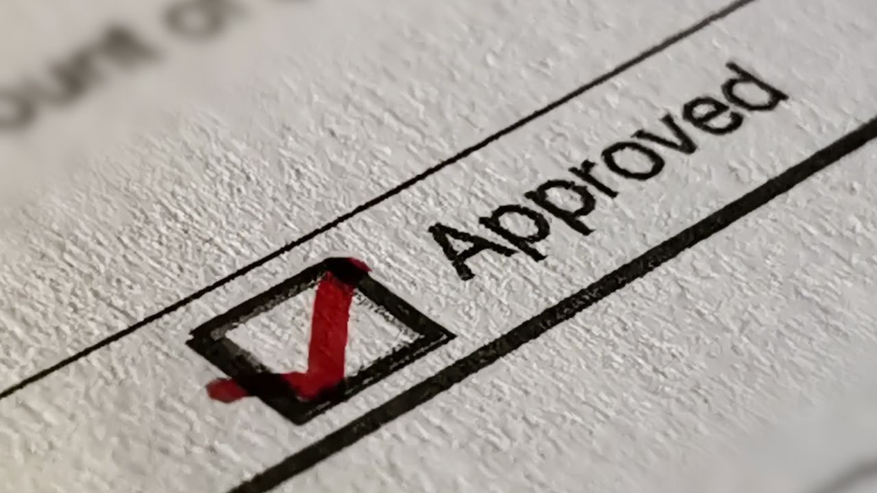 Red checkmark in a square checkbox next to the word 'Approved' on a form or document field.