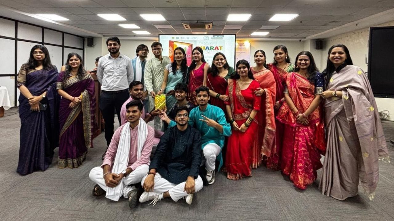 Group of students in colorful sarees and kurtas posing for a cultural event indoors.