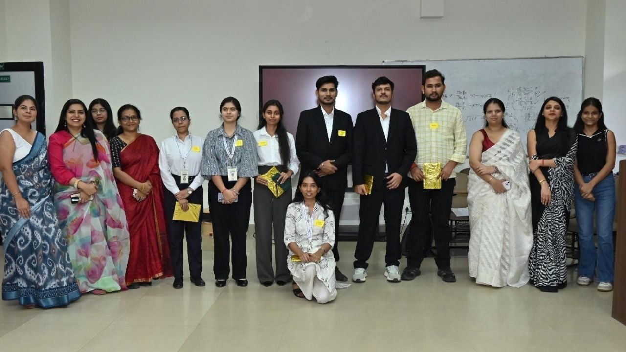 Group of students and professionals posing for a photo at a formal event, with several wearing badges and holding yellow envelopes or folders.