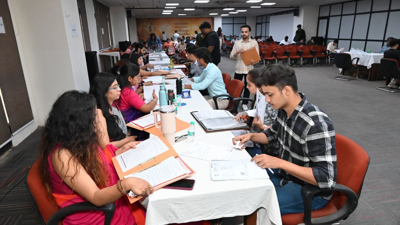 Group of people seated around a long table, reviewing documents and forms at a workshop in a bright conference room, with water bottles and folders visible.