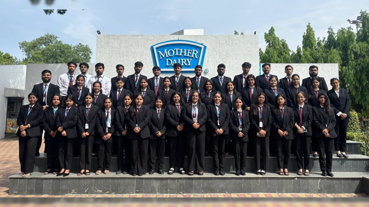 Group of professionals in black suits posing on steps outside a Mother Dairy sign.