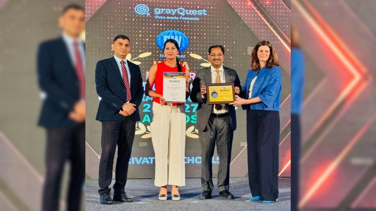 Four professionals on a stage at an awards ceremony; the woman in red holds a certificate and the man beside her holds a plaque, flanked by another man and a woman in business attire.