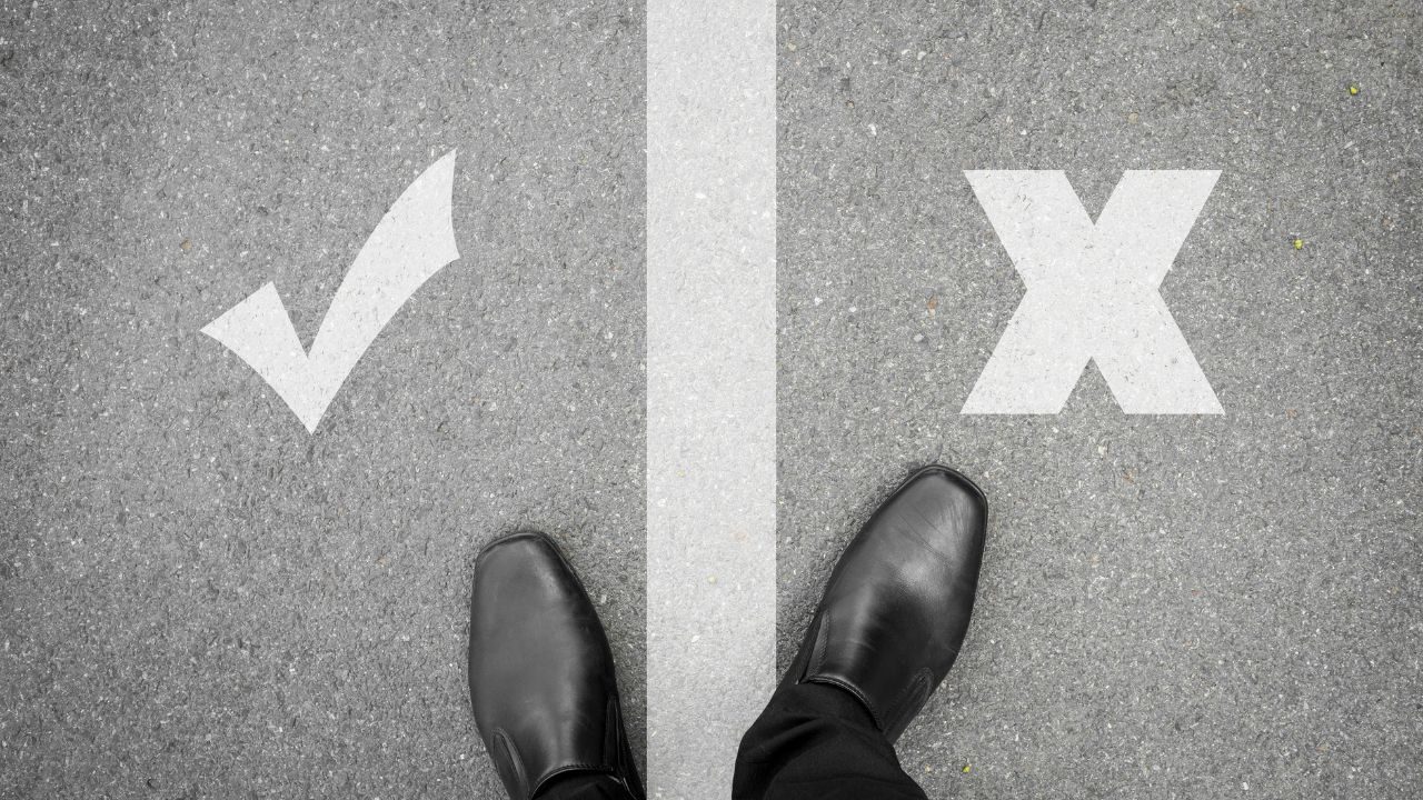 Feet on pavement between a white checkmark on the left and a white X on the right, symbolizing a yes/no choice.
