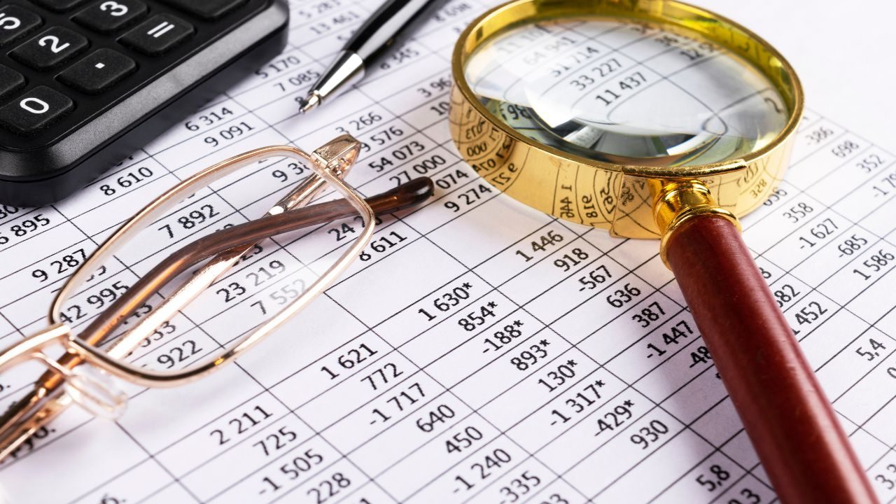 Close-up of a financial worksheet with numbers, a magnifying glass, glasses, and a calculator.