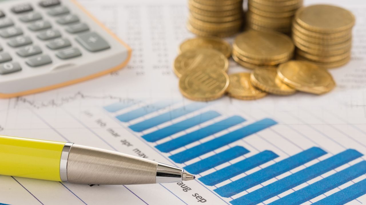 Blue bar chart on a finance report with a yellow pen and stacks of coins nearby, indicating budgeting data