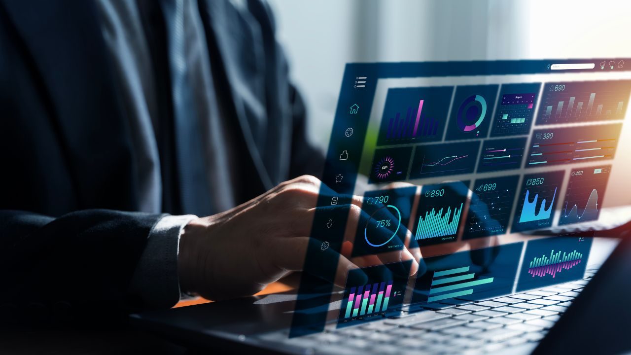 Businessperson in a suit analyzes colorful data dashboards projected over a laptop screen.