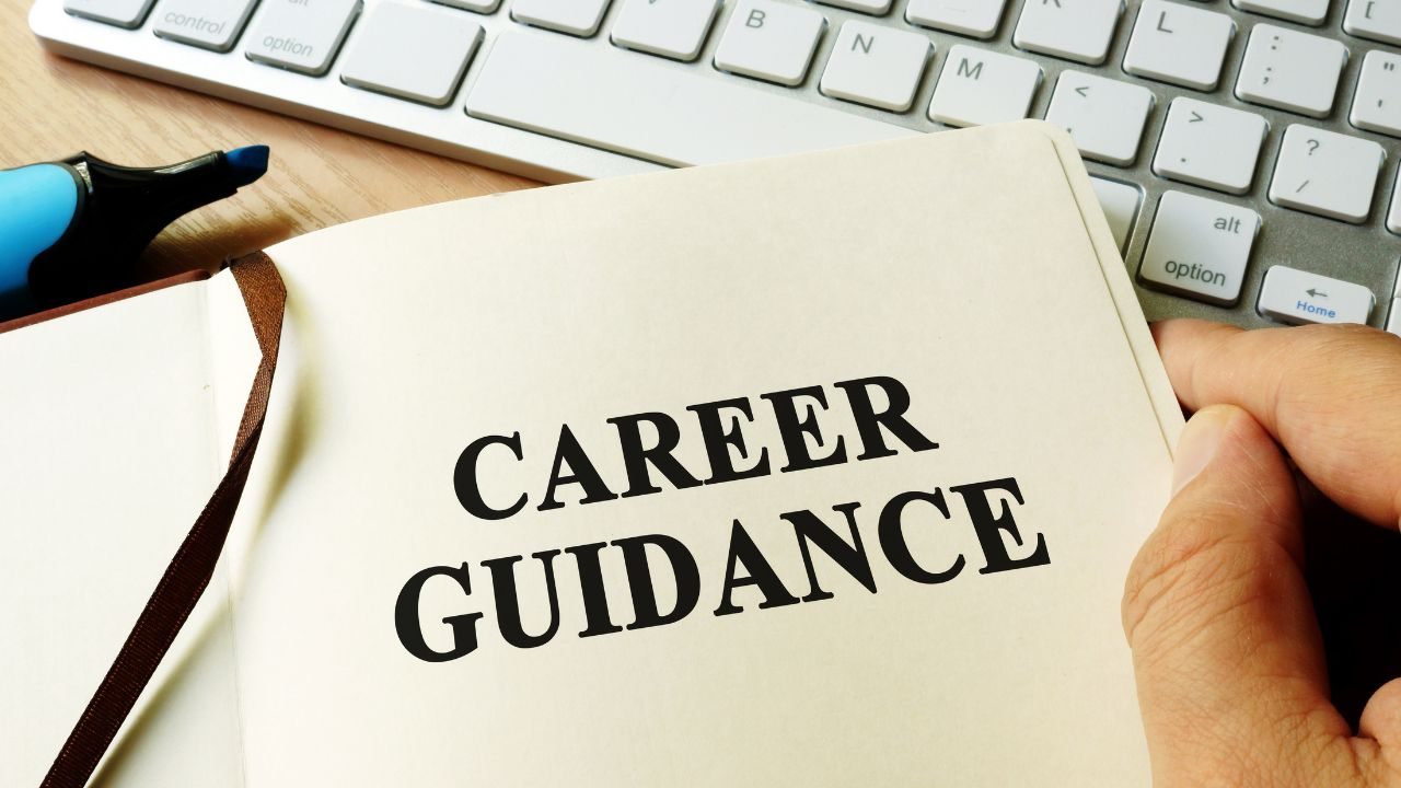 Open notebook page with bold text 'CAREER GUIDANCE' beside a blue marker and a keyboard in the background, conveying career guidance.