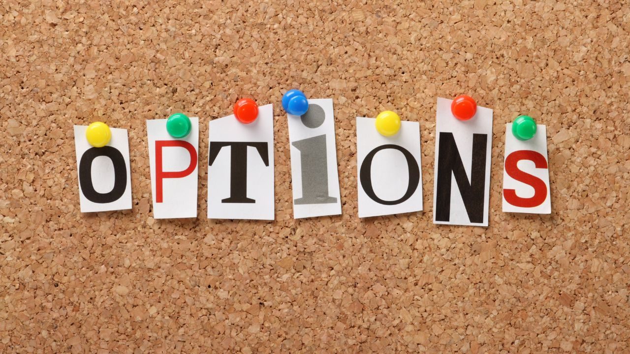 Letters spelling OPTIONS pinned to a corkboard with colorful push pins, suggesting choices or settings.