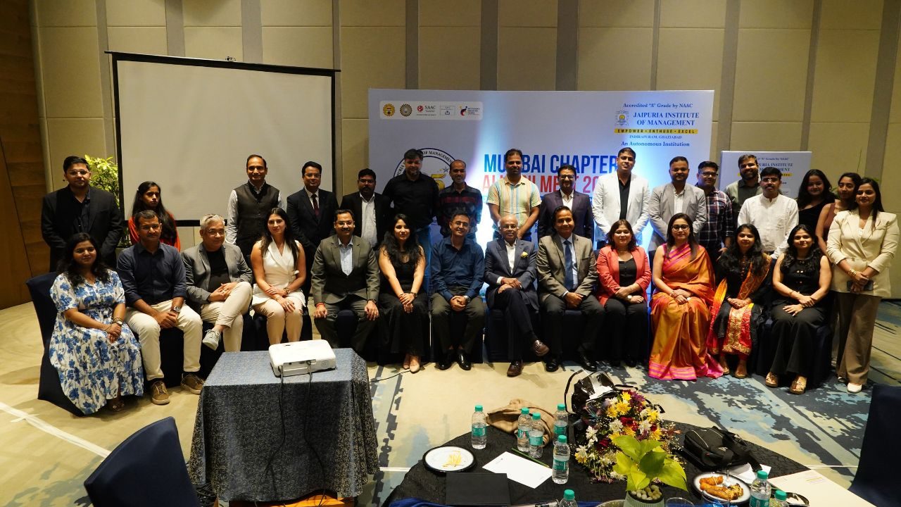 Group photo of professionals in formal attire posing in a conference room, with a banner and projector screen in the background.