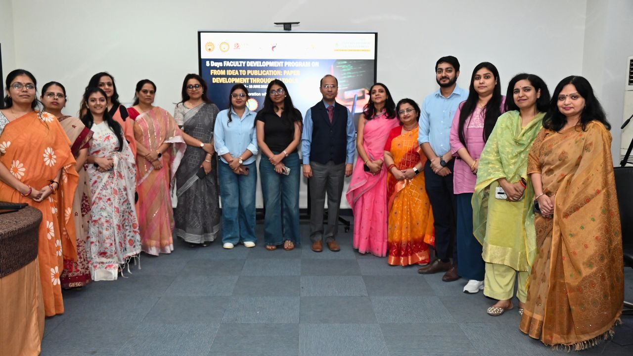 Group of professionals in colorful Indian attire posing for a photo in front of a presentation screen in a conference room.