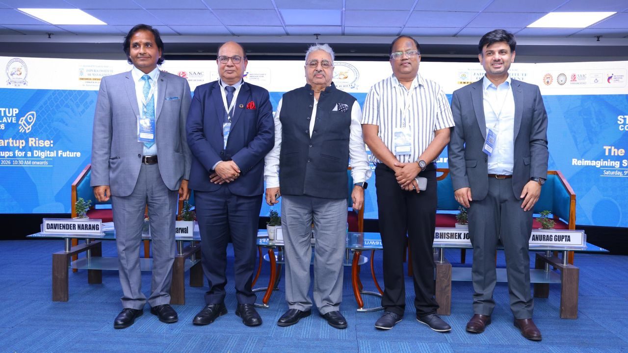 Five men in business attire stand on a stage with a blue conference backdrop, wearing lanyards and name badges for a panel event titled 'Startup Rise: ... for a Digital Future.'